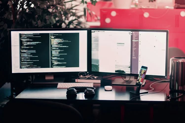 Two monitors on a desk showing code and dashboards
